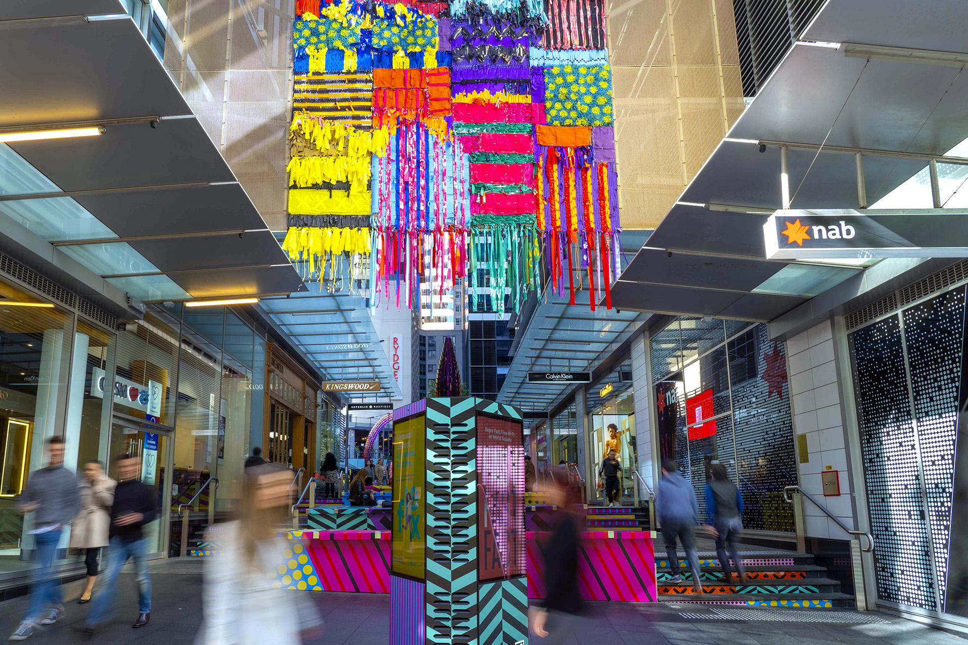 Shoppers enjoying a multicoloured placemaking artistic mural at World Square - a World of Colour by VANDAL