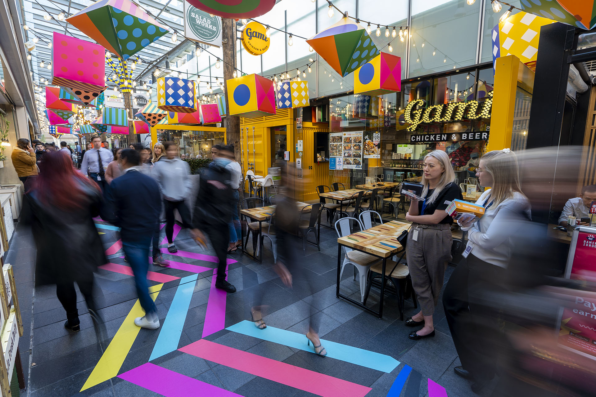 Shoppers enjoying a multicoloured placemaking artistic mural at World Square - a World of Colour by VANDAL