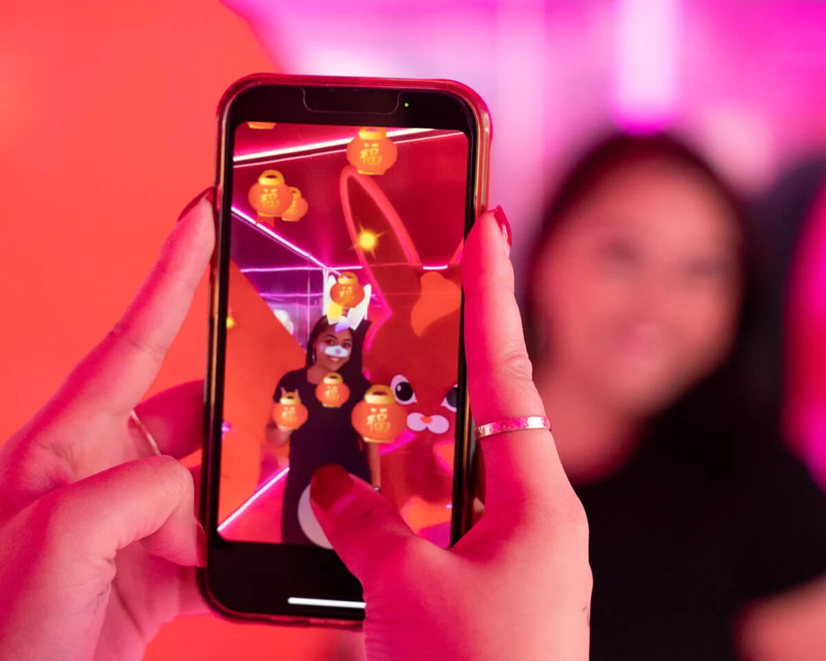 Hands golding a smart phone to take a photo of a woman inside the Lucky Lunar experiential brand activation installation at World Square Sydney for Lunar New Year adorned with VFX rabbit face filters 